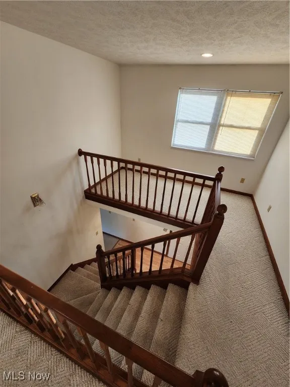 Staircase with carpet floors and a textured ceiling