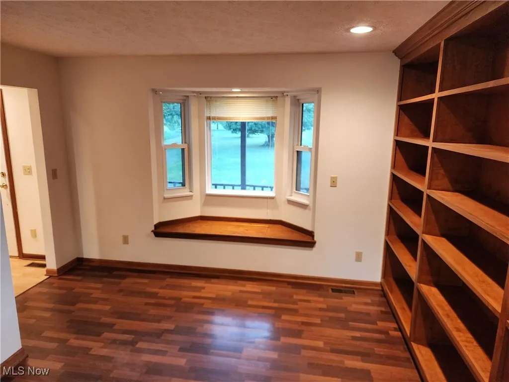 Library with dark Pergo wood-type flooring, bow window with built in cedar chest and recessed lighting