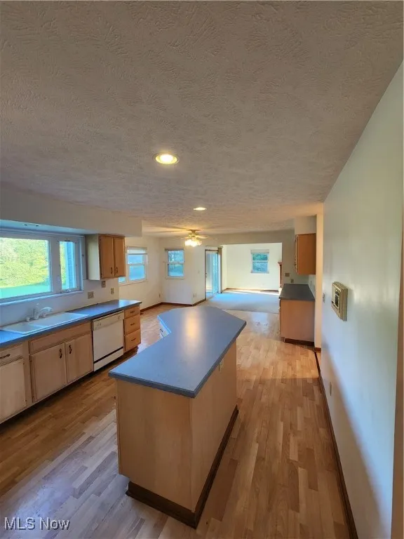 Kitchen with a center island, light Pergo wood-type flooring, open floor plan, a textured ceiling, and dishwashing machine