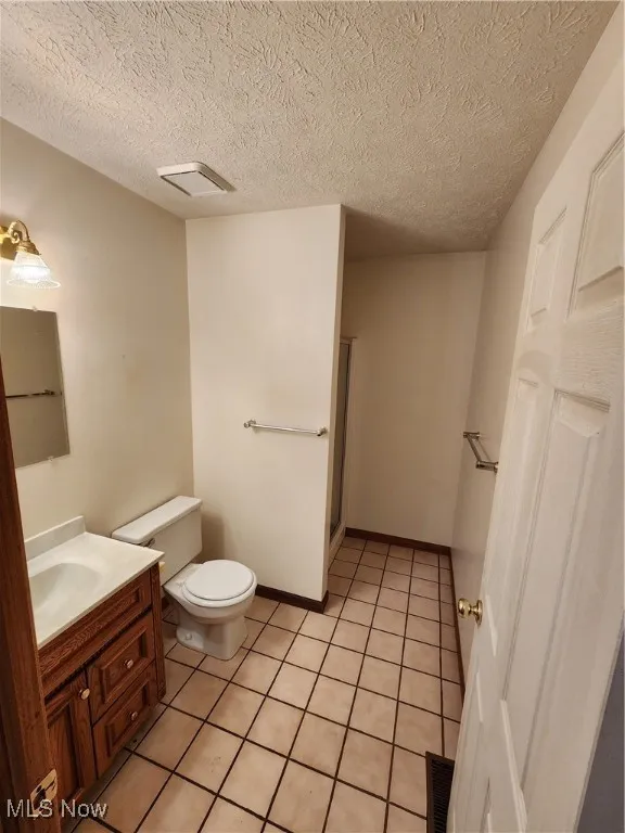 Bathroom with vanity, light tile floors, a textured ceiling, and a shower stall