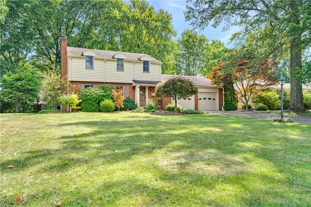 Colonial home with brick siding, a chimney, a front yard, and a garage