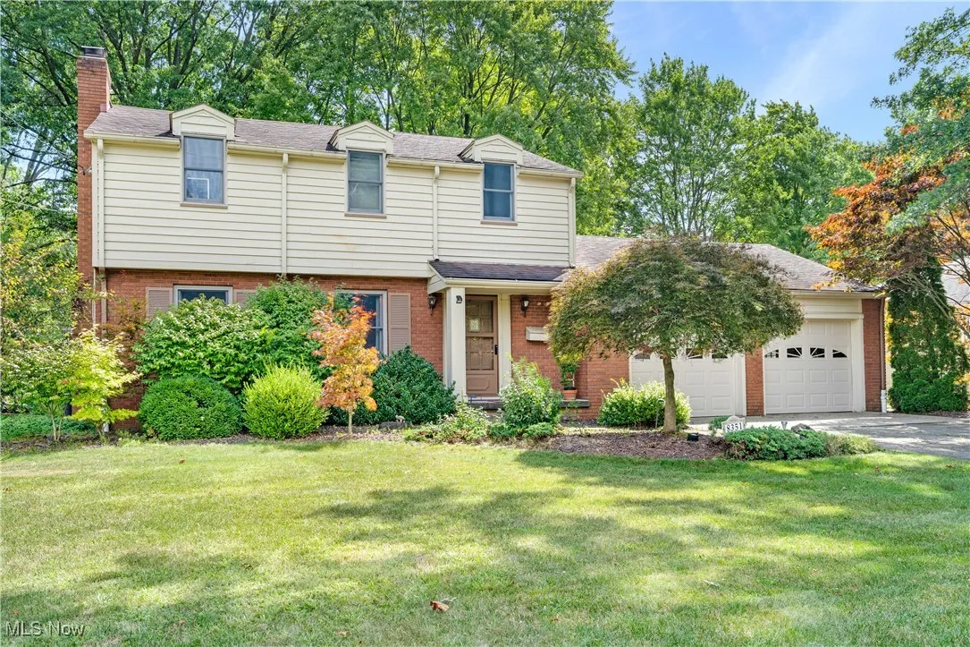 View of front of house featuring a chimney, brick siding, a garage, a front lawn, and asphalt driveway