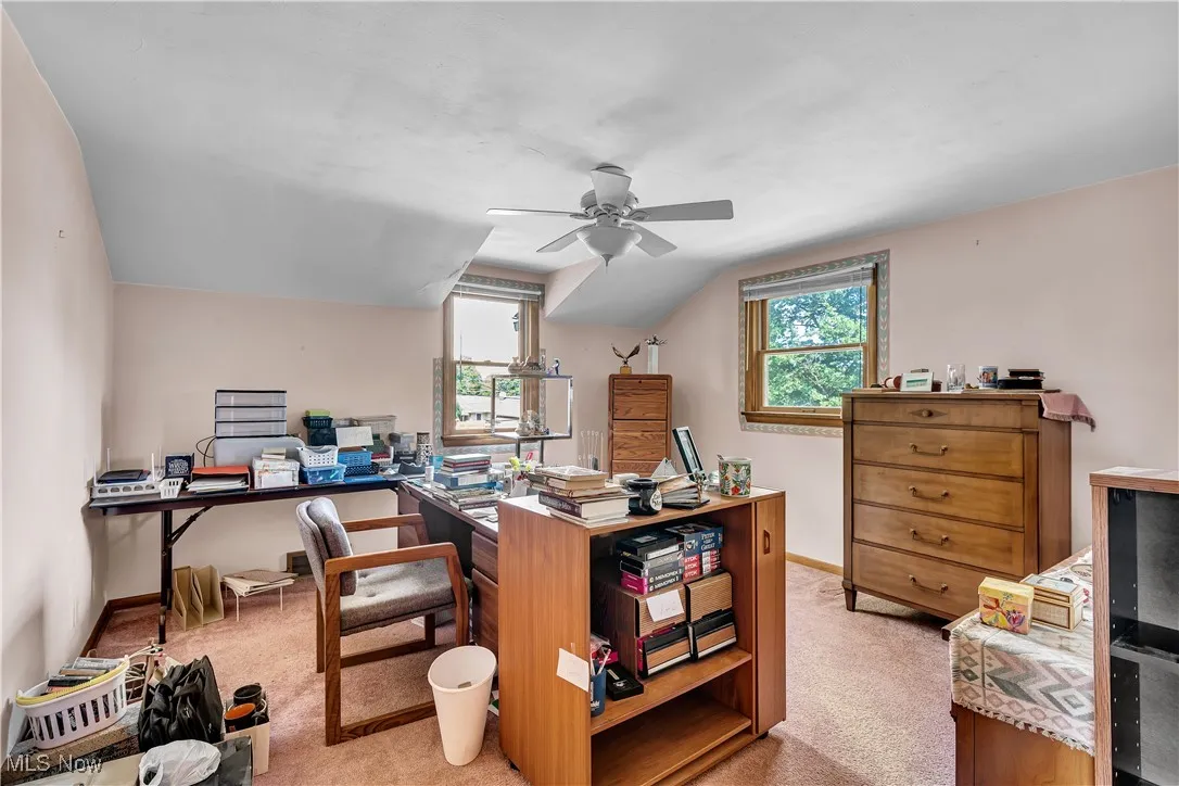 Home office featuring healthy amount of natural light, light colored carpet, ceiling fan, and lofted ceiling
