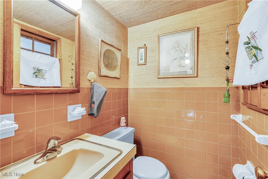 Half bath with vanity, tile walls, and wallpapered walls
