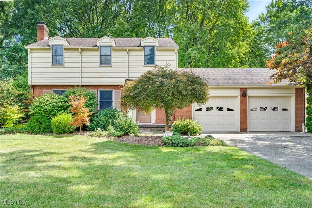 View of front of property featuring brick siding, an attached garage, asphalt driveway, and a chimney