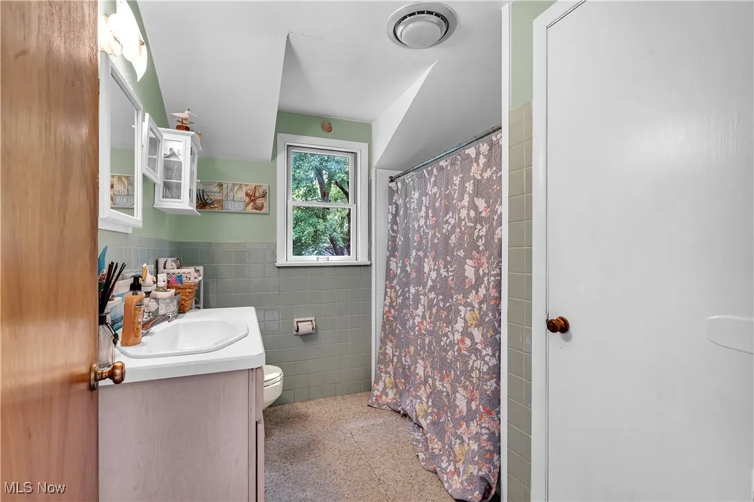 Bathroom featuring tile walls, dark aggregate flooring, vanity, a shower with curtain, and a wainscoted​​‌​​​​‌​​‌‌​‌‌​​​‌‌​‌​‌​‌​​​‌​​ wall
