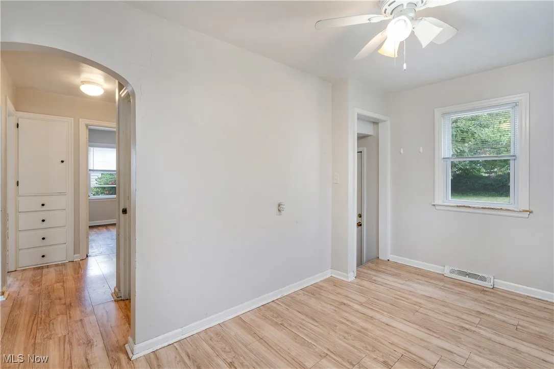 Unfurnished room featuring arched walkways, light wood-style flooring, and a ceiling fan