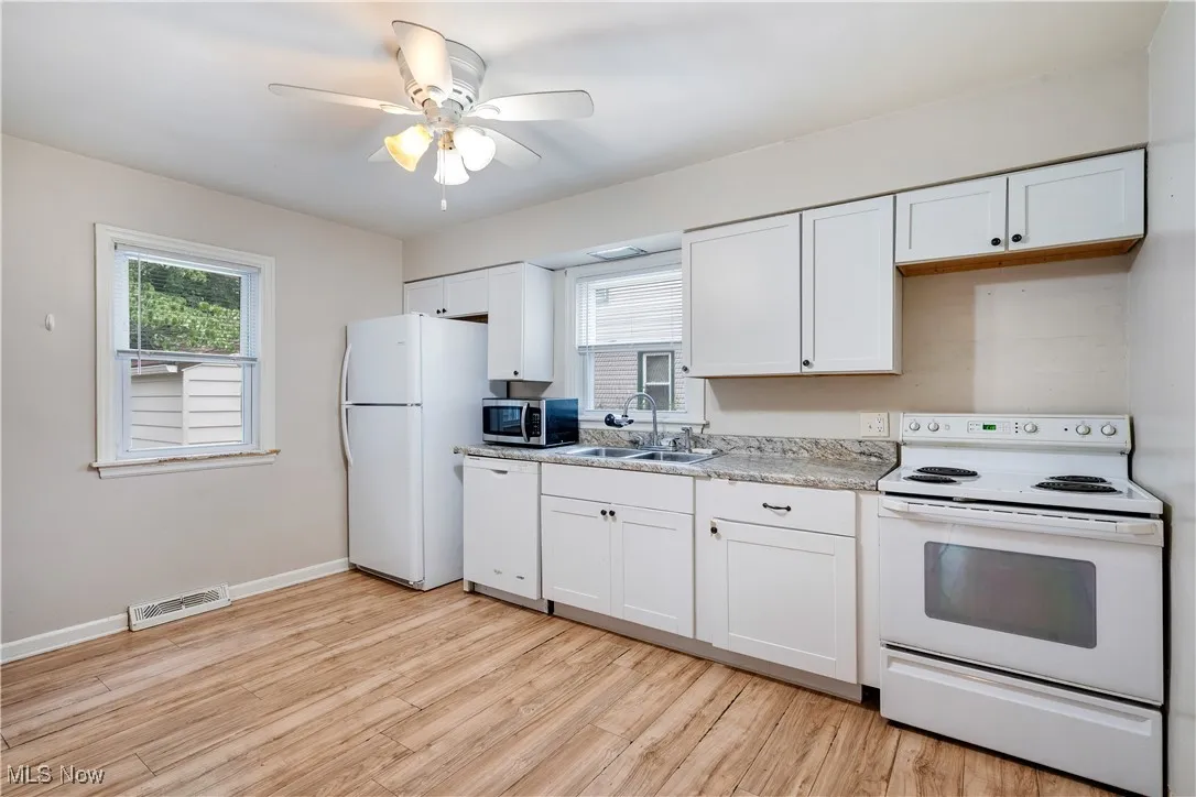 Kitchen with white appliances, white cabinetry, light wood-type flooring, light countertops, and ceiling fan