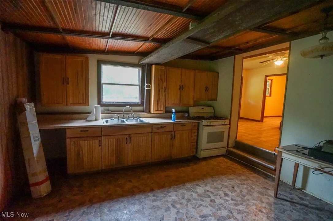 Kitchen with white range with gas cooktop, light countertops, brown cabinetry, and a ceiling fan