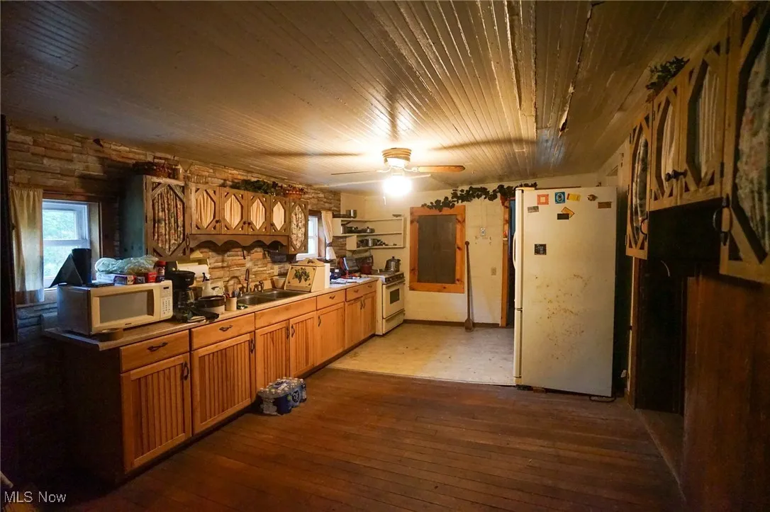 Kitchen featuring dark wood-type flooring, white appliances, light countertops, a ceiling fan, and brown cabinets