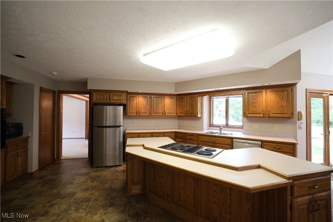 Kitchen featuring light countertops, brown cabinetry, appliances with stainless steel finishes, stone finish floors, and a center island