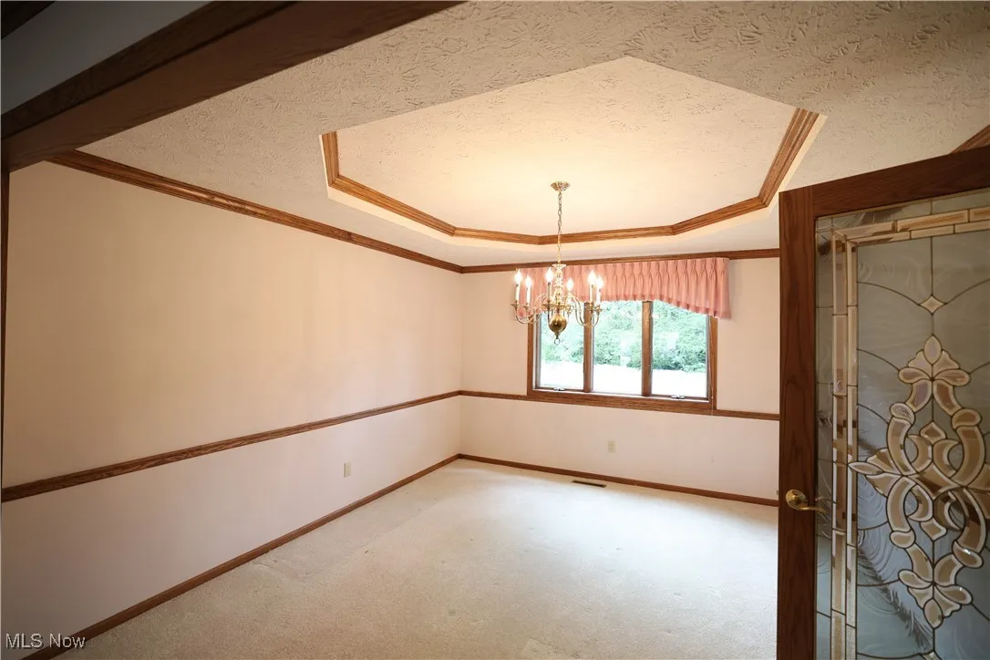 Formal dining room with crown molding, tray ceiling, a chandelier, and carpet floors