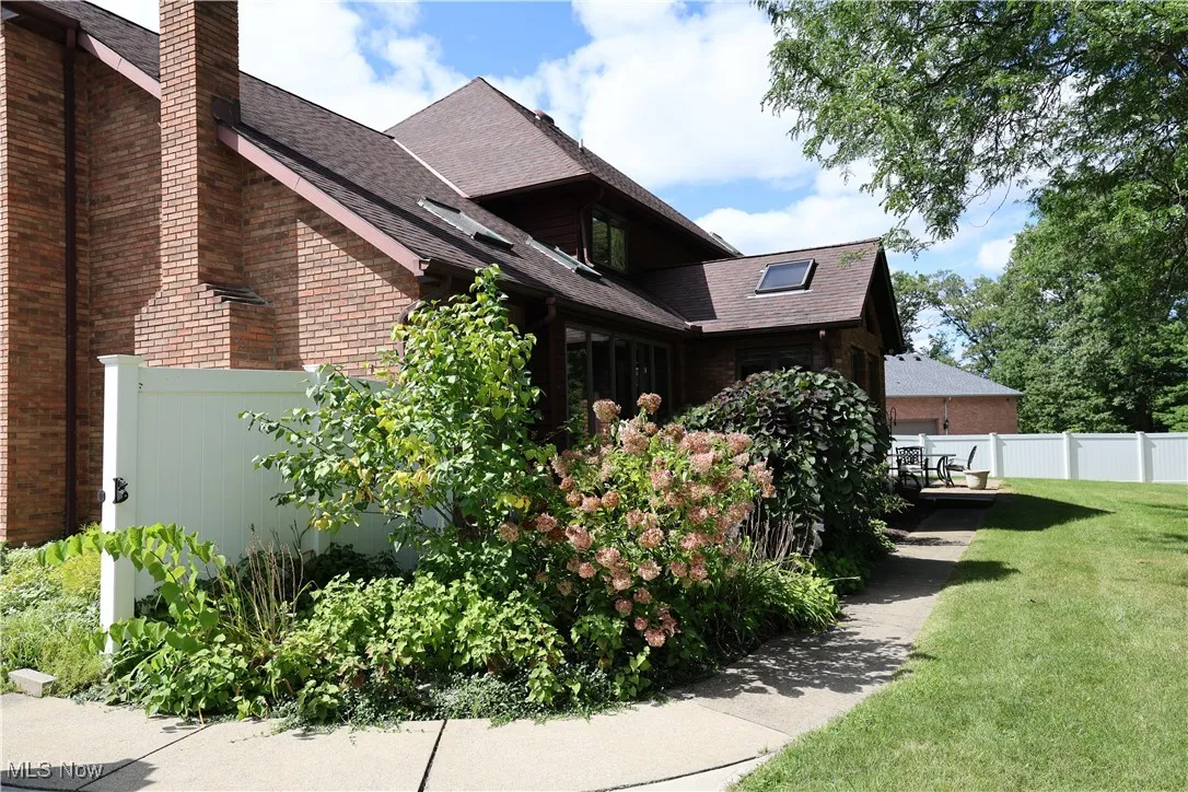 View of home's exterior featuring lush landscaping, brick siding, a chimney, a shingled roof, and concrete walkway to patio