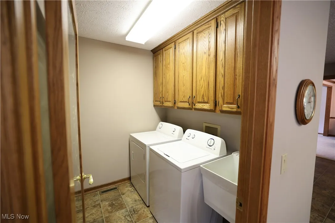 Laundry room with a textured ceiling, cabinet space, washer and clothes dryer, and vinyl flooring