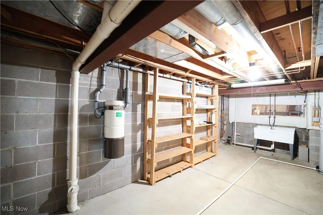 View of unfinished basement with central vacuum, shelving and double utility sink