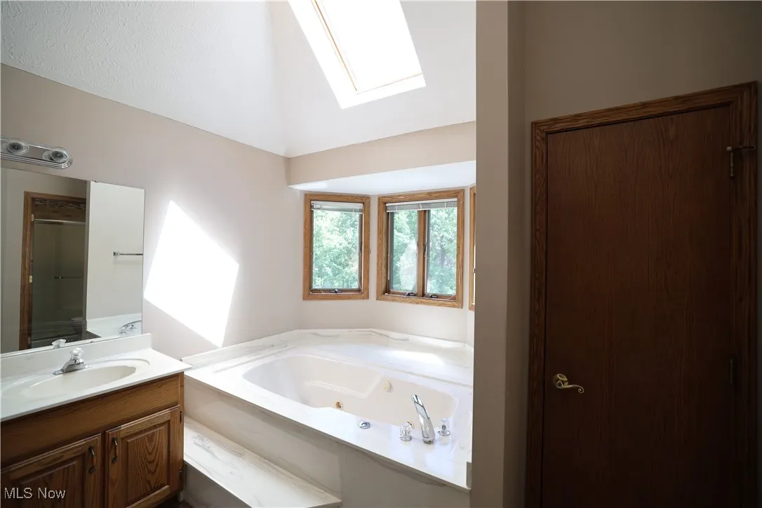 Primary bathroom featuring dual vanity, jacuzzi tub, a skylight, and vaulted ceilings
