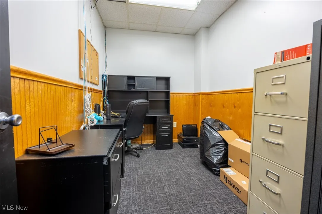 Home office with a wainscoted wall, a drop ceiling, wood walls, and dark colored carpet