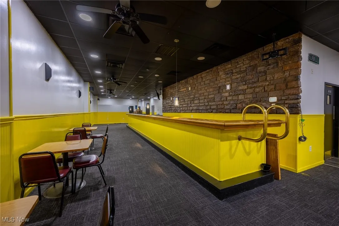 View of community featuring a paneled ceiling, brick wall, wainscoting, and ceiling fan