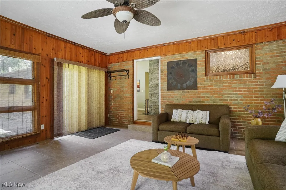 Tiled living area featuring ornamental molding, wooden walls, a ceiling fan, and a textured ceiling