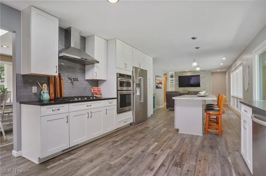 Kitchen featuring white cabinetry, recessed lighting, open floor plan, wall chimney exhaust hood, and pendant lighting
