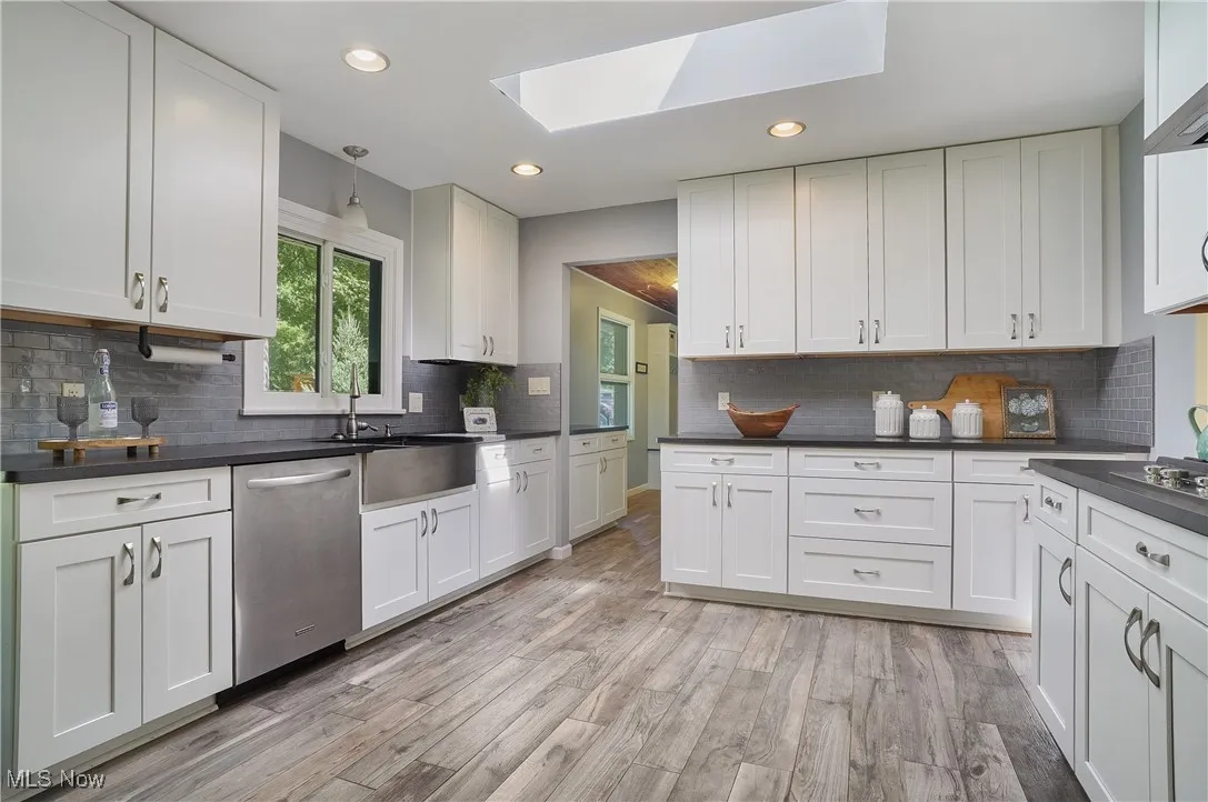 Kitchen featuring a skylight, dishwasher, white cabinets, light wood finished floors, and recessed lighting