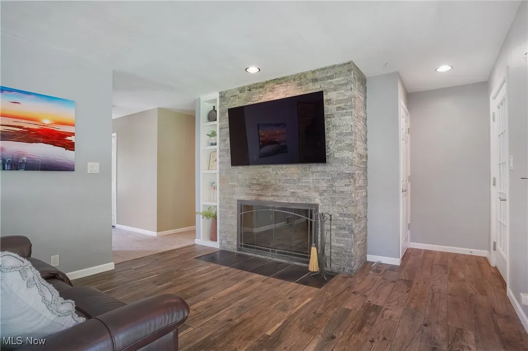 Living room featuring dark wood-style flooring, a fireplace, recessed lighting, and built in shelves