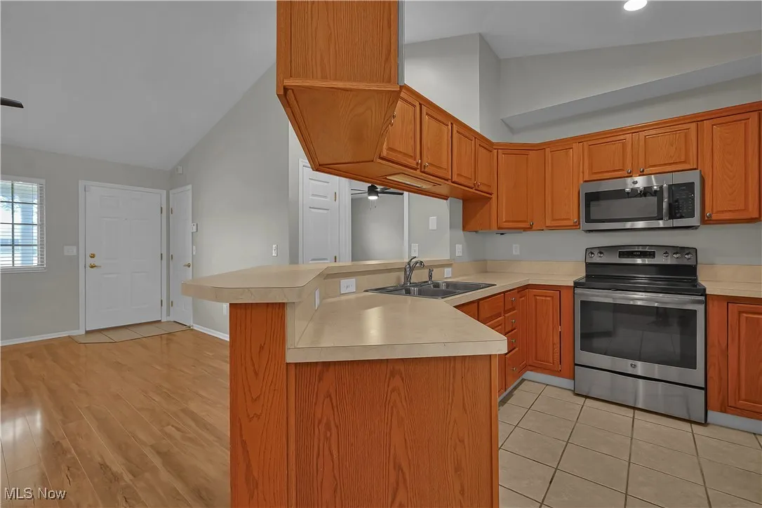 Kitchen with a peninsula, stainless steel appliances, light countertops, brown cabinets, and ceiling fan