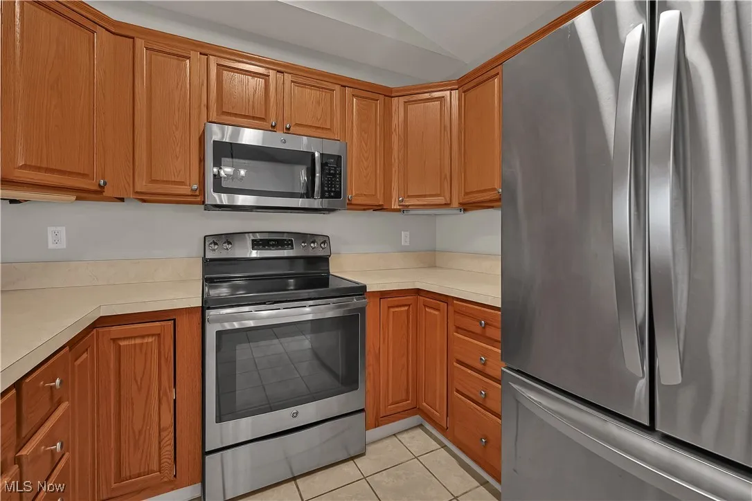 Kitchen with appliances with stainless steel finishes, light countertops, light tile patterned floors, brown cabinetry, and lofted ceiling
