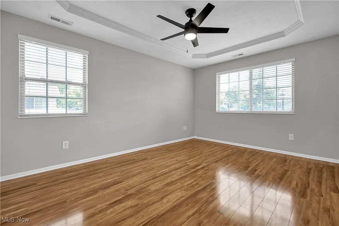 Empty room with a raised ceiling, wood finished floors, and a ceiling fan