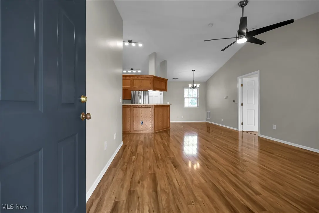 Unfurnished living room with dark wood-type flooring, vaulted ceiling, a ceiling fan, and a chandelier