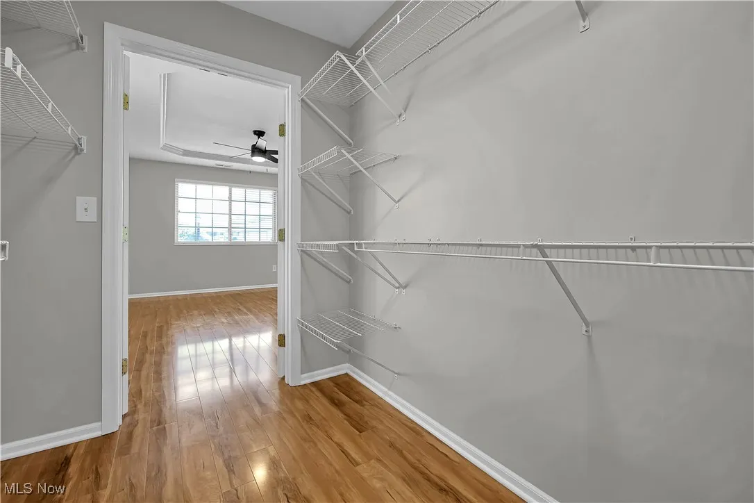 Walk in closet with light wood finished floors and a ceiling fan
