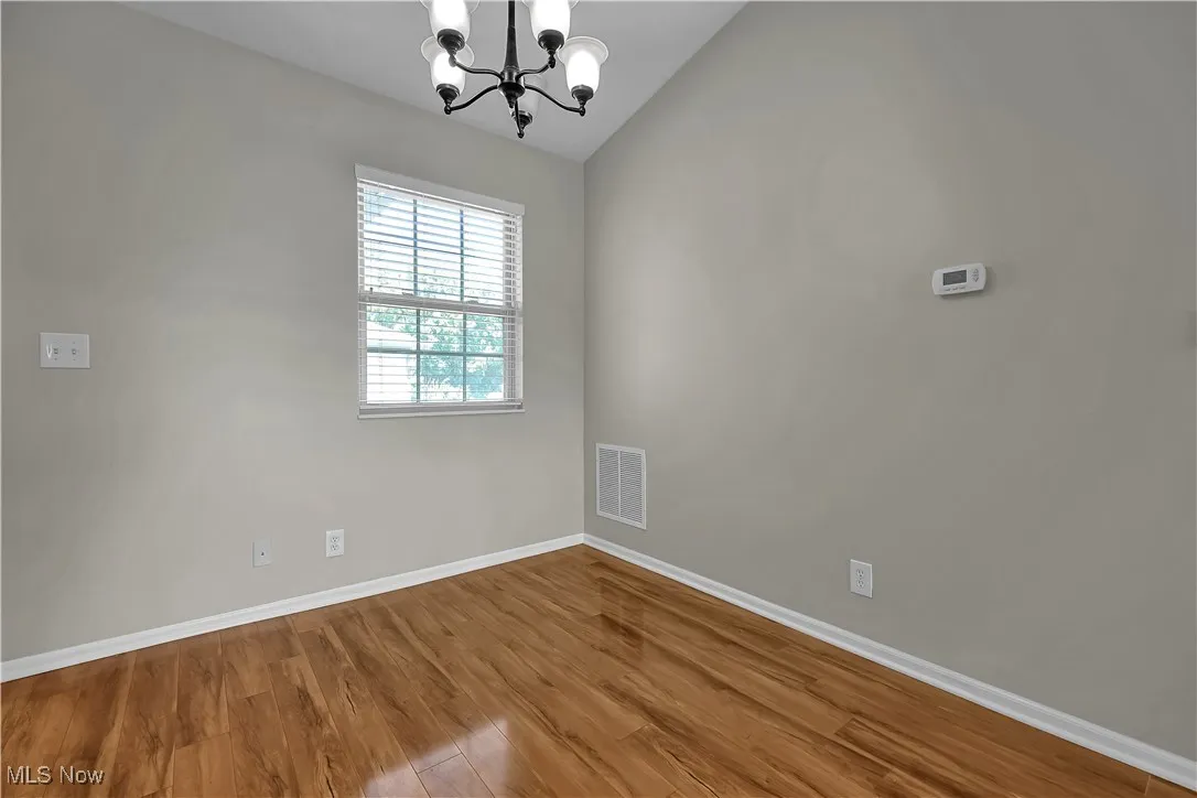 Unfurnished room with wood finished floors, a chandelier, and vaulted ceiling