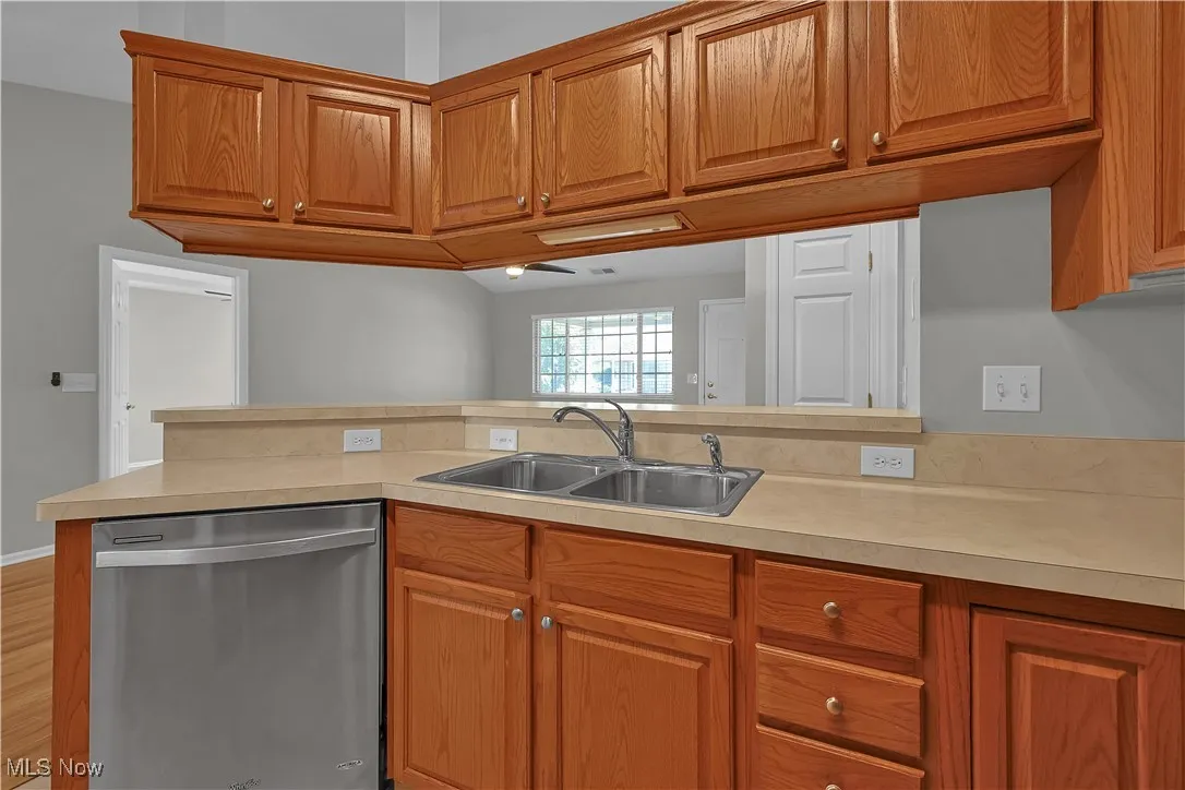 Kitchen featuring dishwasher, brown cabinetry, light countertops, light wood-style flooring, and a peninsula