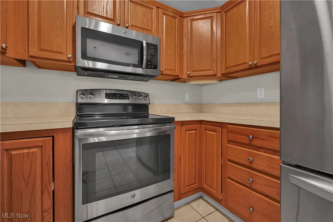 Kitchen featuring appliances with stainless steel finishes, light countertops, brown cabinets, and light tile patterned flooring
