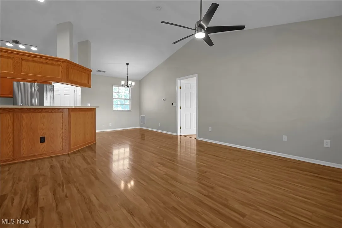 Unfurnished living room with light wood-style floors, a chandelier, a ceiling fan, and high vaulted ceiling