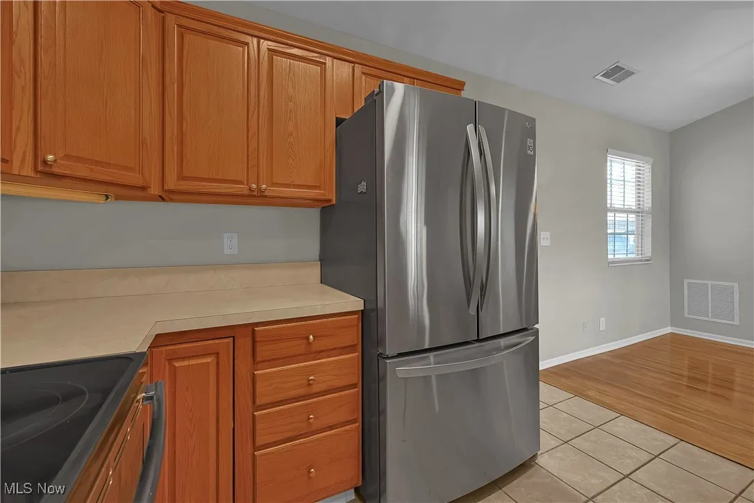 Kitchen featuring black range with electric stovetop, freestanding refrigerator, light tile patterned flooring, light countertops, and brown cabinetry