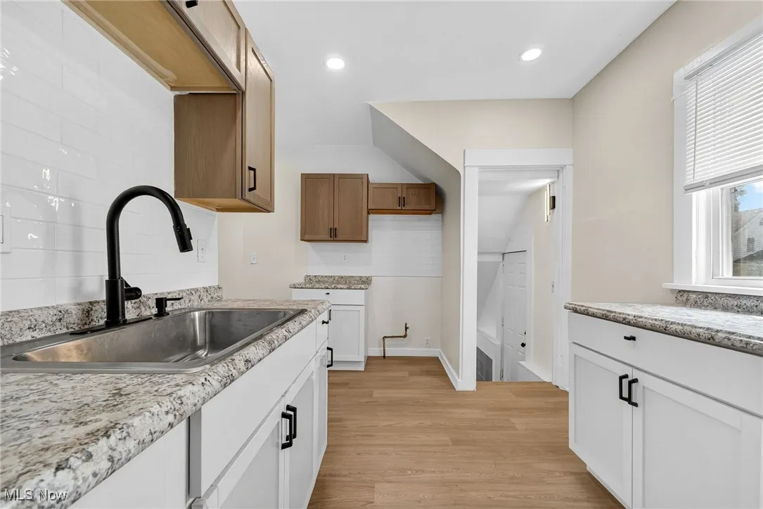 Kitchen with light wood-style flooring, decorative backsplash, recessed lighting, light stone counters, and brown cabinetry