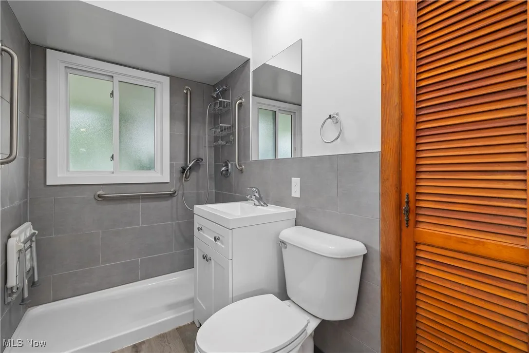 Full bathroom featuring a closet, vanity, a shower stall, and tile walls