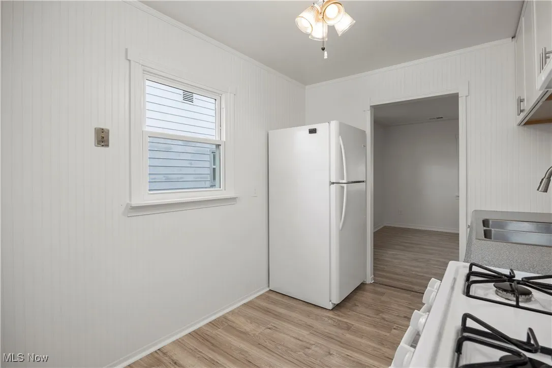 Kitchen featuring white appliances, light wood-style flooring, crown molding, and white cabinetry