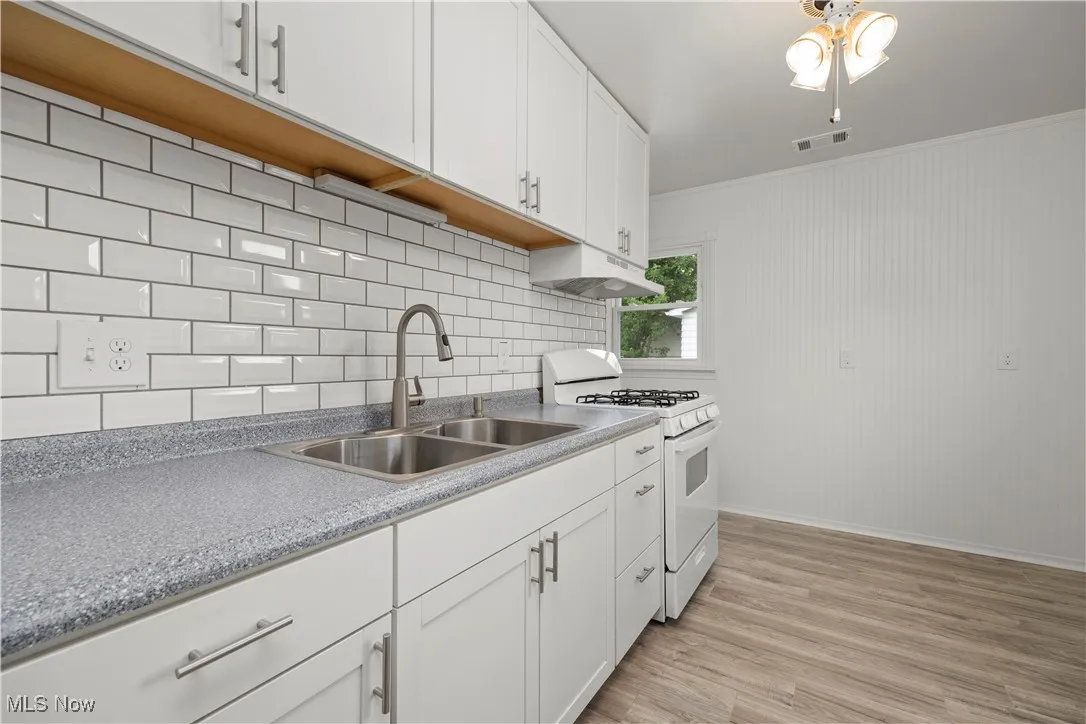 Kitchen with gas range gas stove, white cabinets, light wood-style flooring, tasteful backsplash, and under cabinet range hood