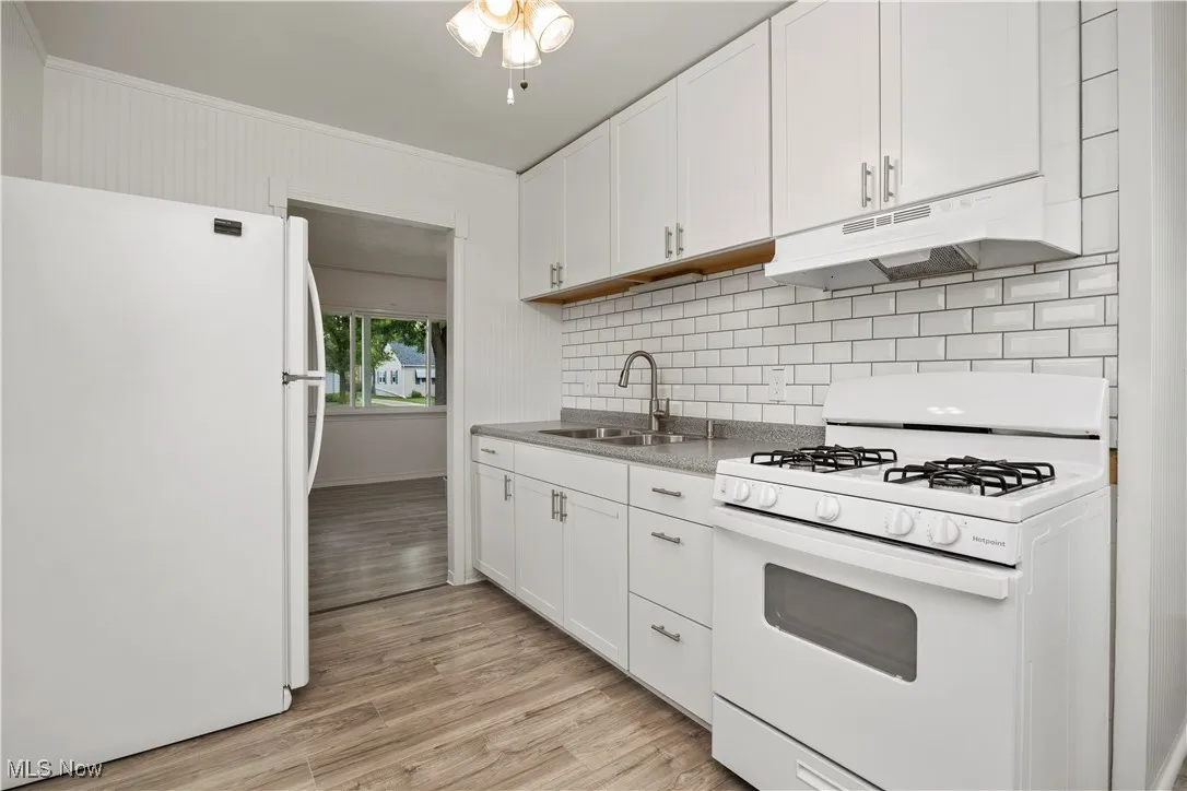 Kitchen featuring white appliances, under cabinet range hood, white cabinetry, light wood-style floors, and crown molding