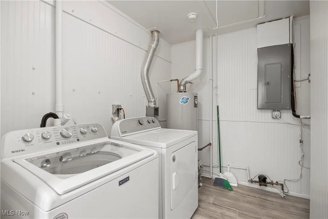 Laundry room with light wood-style flooring, electric panel, washer and clothes dryer, and water heater