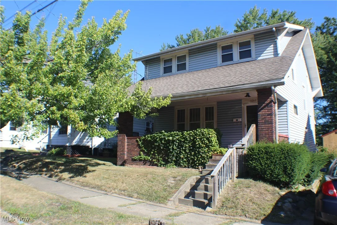 View of front facade featuring covered porch, roof with shingles, and a front yard