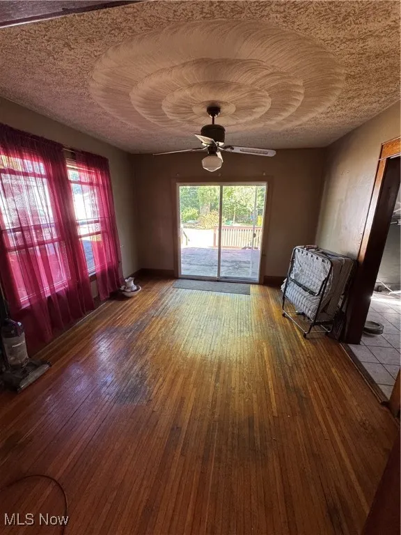 Unfurnished living room with hardwood / wood-style flooring, plenty of natural light, a textured ceiling, heating unit, and ceiling fan