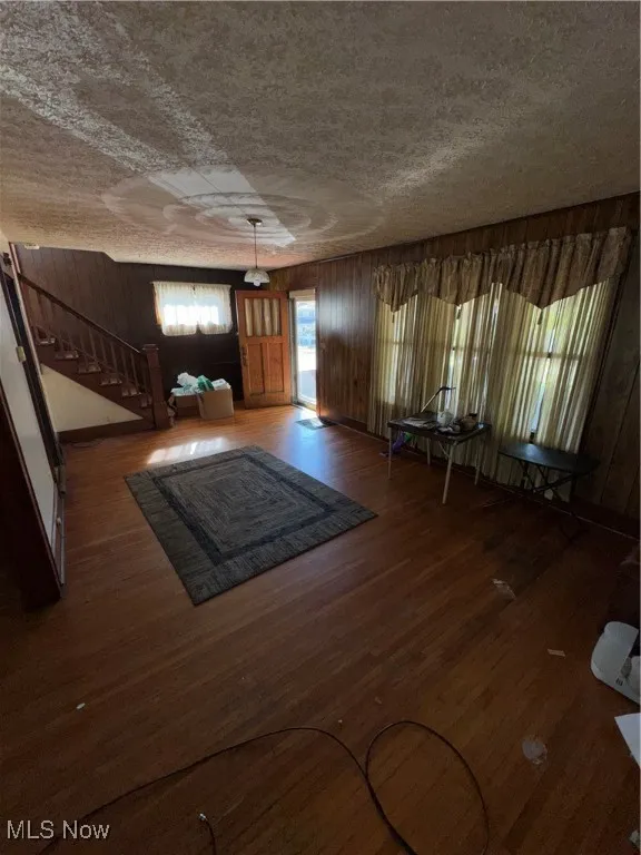Foyer entrance with wood finished floors, wood walls, a textured ceiling, and stairs