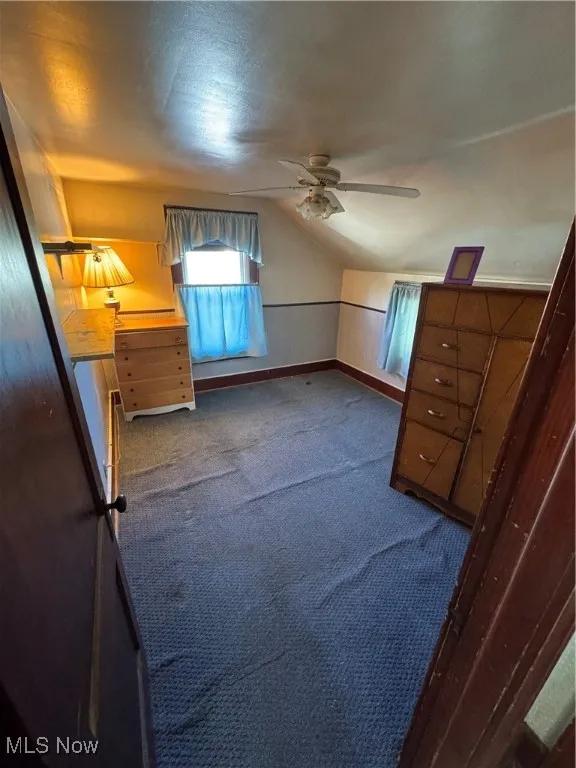 Unfurnished bedroom featuring a ceiling fan, vaulted ceiling, and carpet flooring