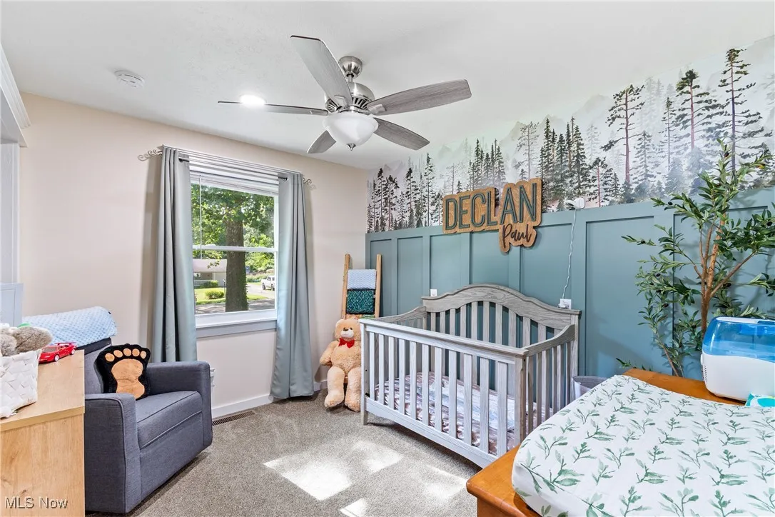 Carpeted bedroom featuring a nursery area and a ceiling fan