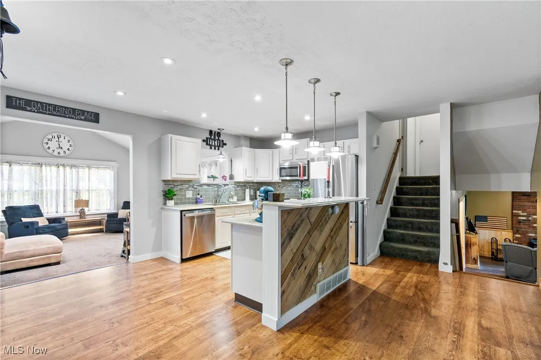 Kitchen featuring open floor plan, white cabinetry, backsplash, a kitchen island, and hanging light fixtures