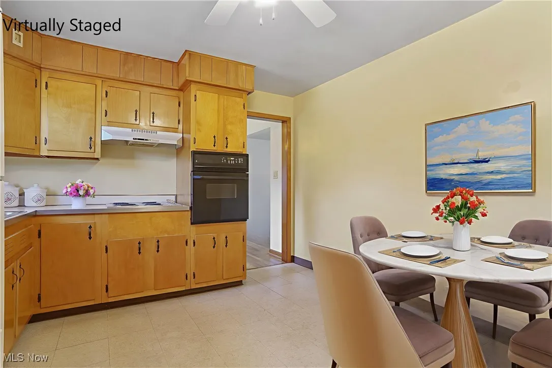 Kitchen featuring black oven, light countertops, under cabinet range hood, a ceiling fan, and light flooring