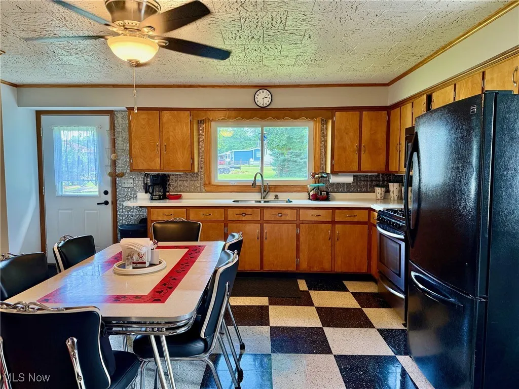 Kitchen with dark floors, freestanding refrigerator, light countertops, brown cabinetry, and stainless steel gas stove